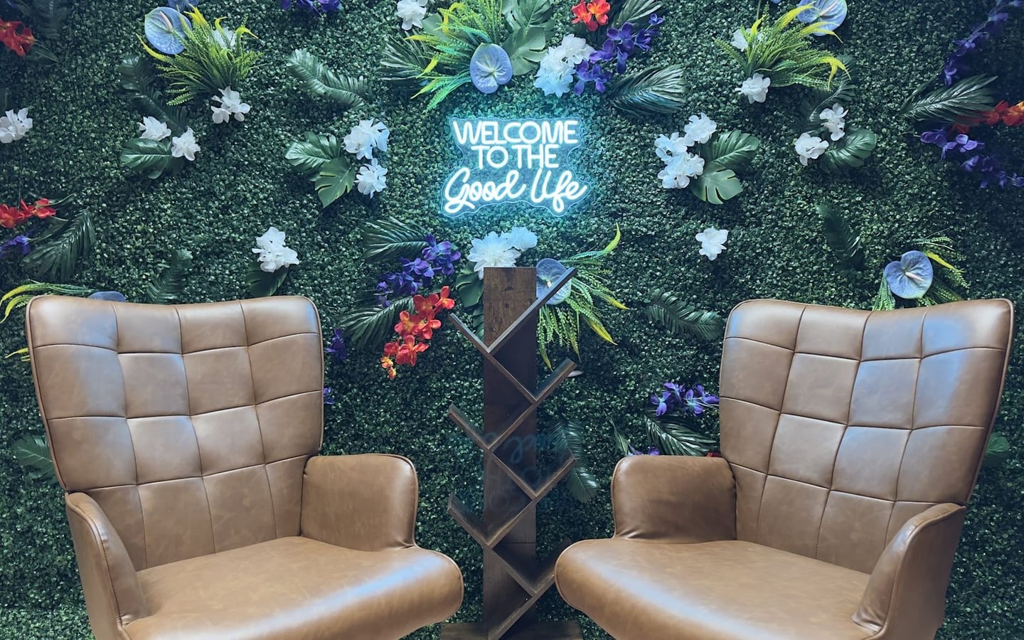 The Good Life: two tufted armchairs in front of a living moss wall with a neon script sign